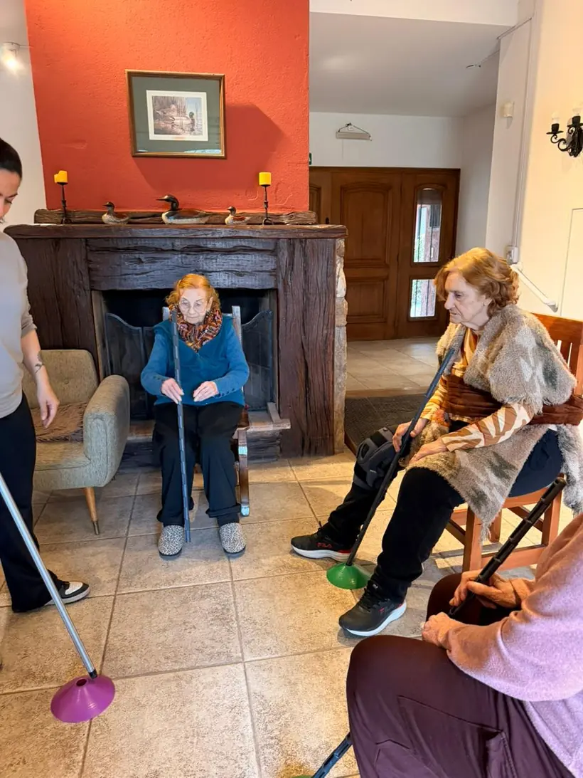 Residentes sentadas en ronda en el living jugando con bastones y aros, junto al hogar a leña