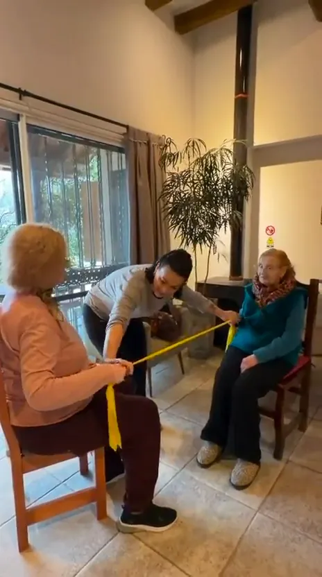 Residentes haciendo gimnasia sentadas, con bandas elásticas, acompañadas por una profesora