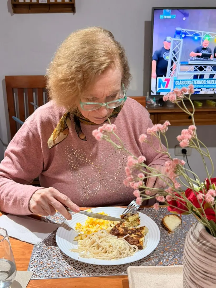 Residente almorzando en la mesa del comedor: fideos, tortilla y un budín casero